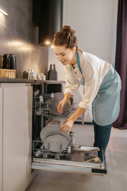 Bulaşık makinesinin yanında duran ve tabakları çıkaran kadın.