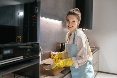 Önlüklü ev hanımı ve bulaşıkları yıkayan sarı eldivenli.