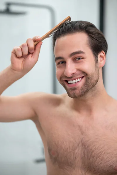 Sorrindo homem fazendo penteado e olhando satisfeito — Fotografia de Stock