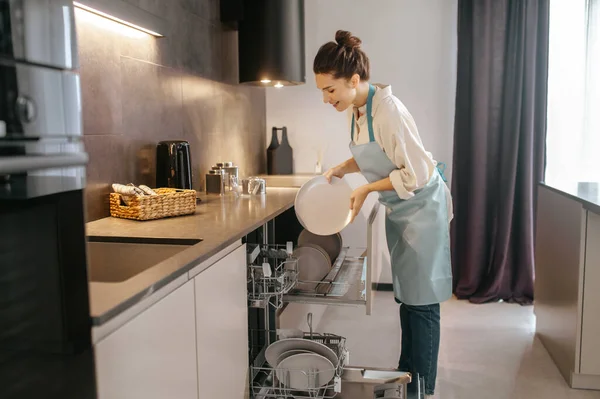 Жінка стоїть біля посудомийної машини і виймає тарілки — стокове фото