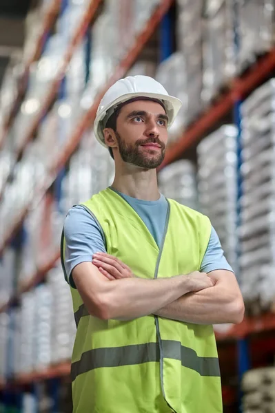 Katlanmış elleri olan kasklı bir adam yana bakıyor.