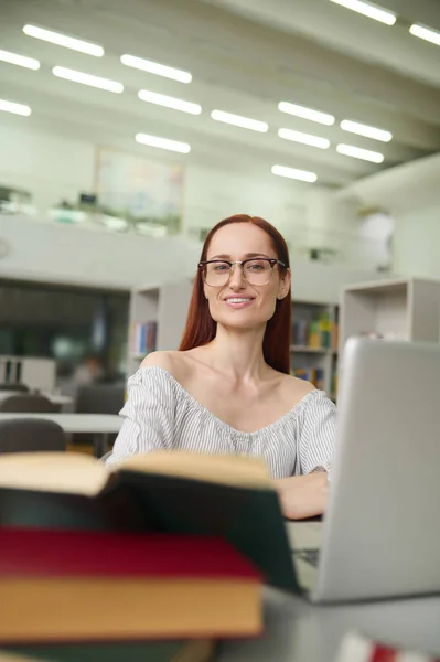 戴眼镜、拿着手提电脑在桌边工作的女人 — 图库照片