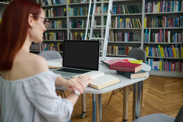 Ноутбук на столе, а женщина читает книгу — стоковое фото