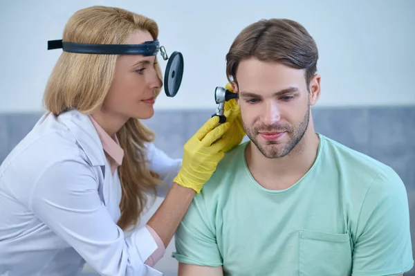 Woman otolaryngologist examining ear of middle aged man — Stock Photo, Image