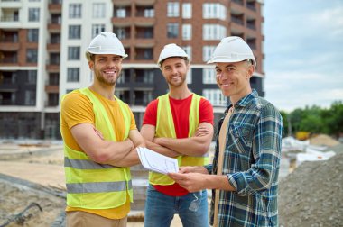 Çizimli bir mühendis ve inşaat alanında iki işçi.