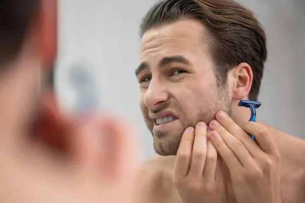 Young man shaving and looking disturbed — Stockfoto