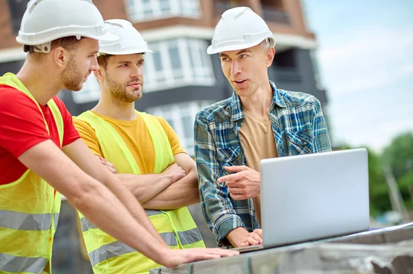 Mérnök és két munkás beszélget laptop közelében szabadban — Stock Fotó