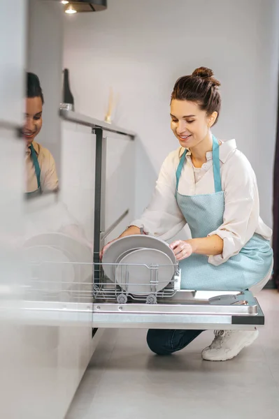Домогосподарка в фартусі заповнює посудомийну машину — стокове фото