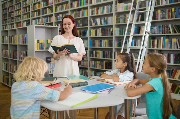 Frau liest Kindern am Tisch Buch vor — Stockfoto