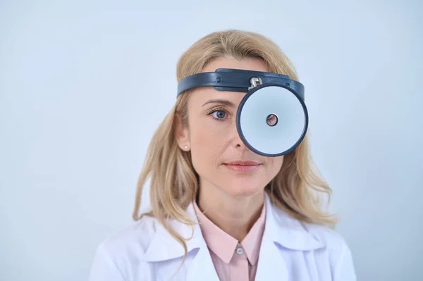 Blonde woman in white coat looking through reflector — Stock Photo, Image