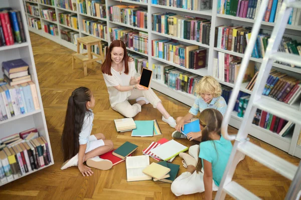 Woman showing tablet to children sitting on floor — Stock Photo, Image