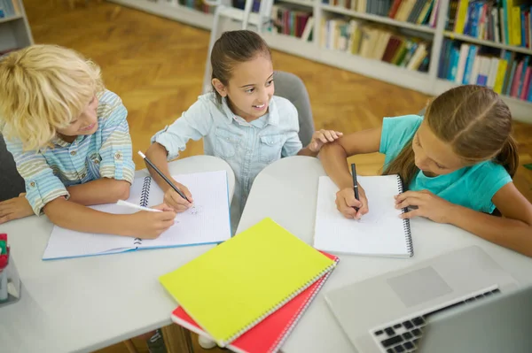 Visão superior de crianças escrevendo à mesa na biblioteca — Fotografia de Stock