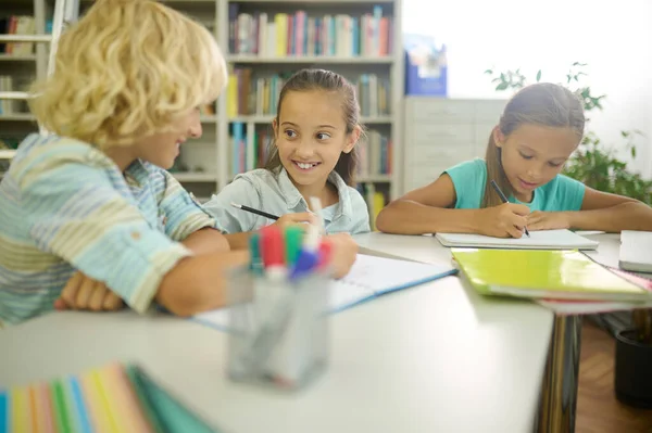 Mädchen schaut Jungen beim Schreiben am Tisch an — Stockfoto