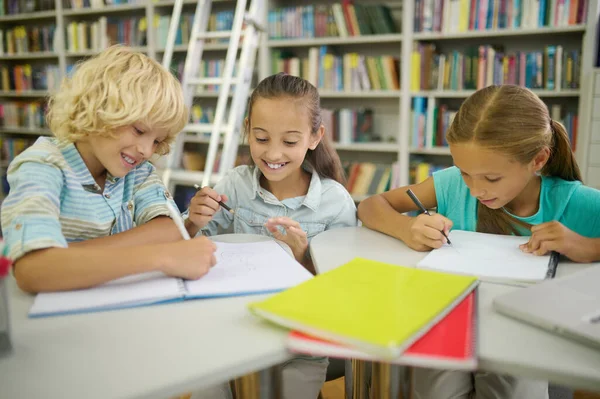 Boy and two girls writing and painting in library — Fotografia de Stock