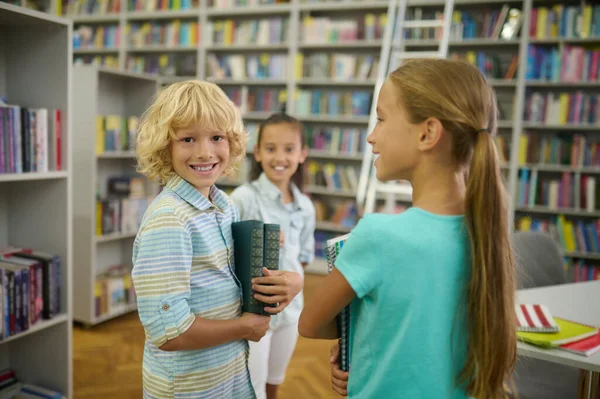 Boy with books looking at camera and two girls — Stock Photo, Image