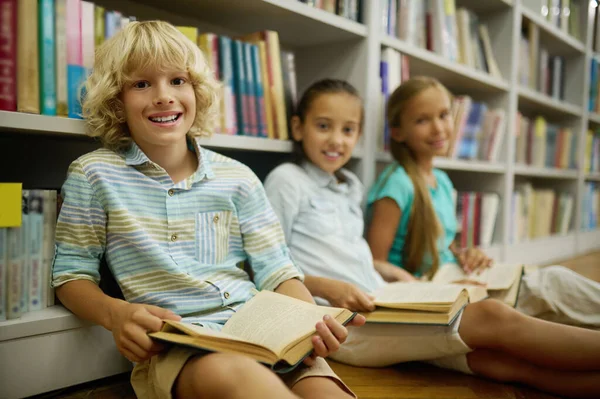 Boy looking at camera sitting on floor with book — Stock Fotó