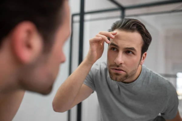 Um jovem de tshirt cinza olhando para seu reflexo no espelho — Fotografia de Stock