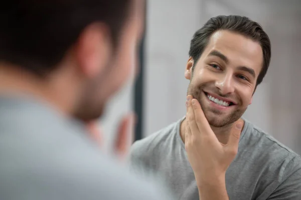 A young man in grey tshirt looking at his reflection in the mirror — Zdjęcie stockowe