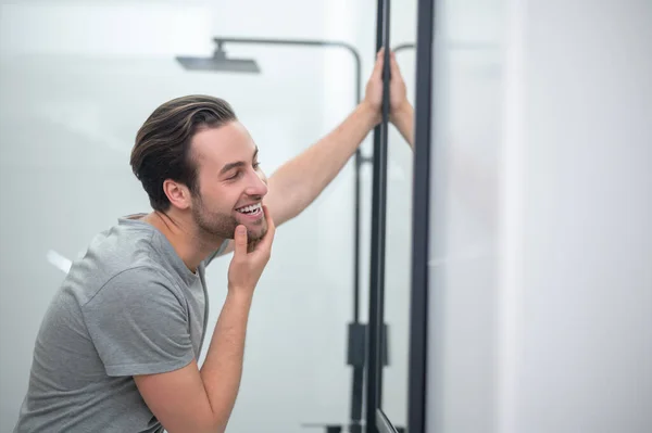 En ung man i grå tröja tittar på sin spegelbild — Stockfoto