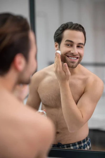 一个半裸的男人站在镜子旁边，把剃须泡沫涂在他的脸上 — 图库照片