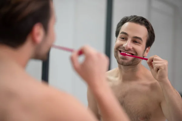 笑顔の若い男は彼の歯を磨くと屈託のない見て — ストック写真