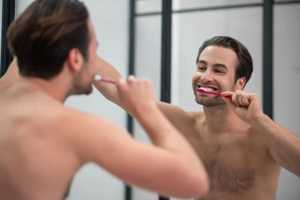 Smiling young man brshing his teeth and looking carefree — Stockfoto