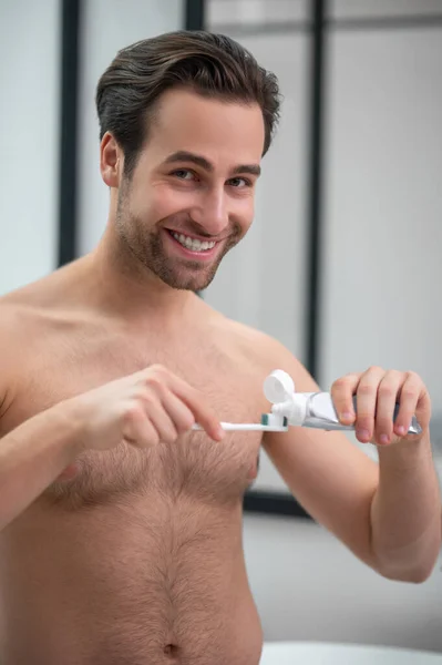 Joven hombre guapo apretando pasta de dientes en un cepillo de dientes —  Fotos de Stock