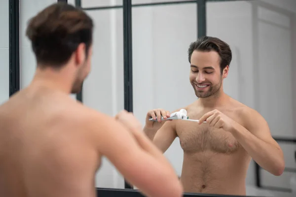 Молодой красивый мужчина сжимает зубную пасту на зубной щетке — стоковое фото