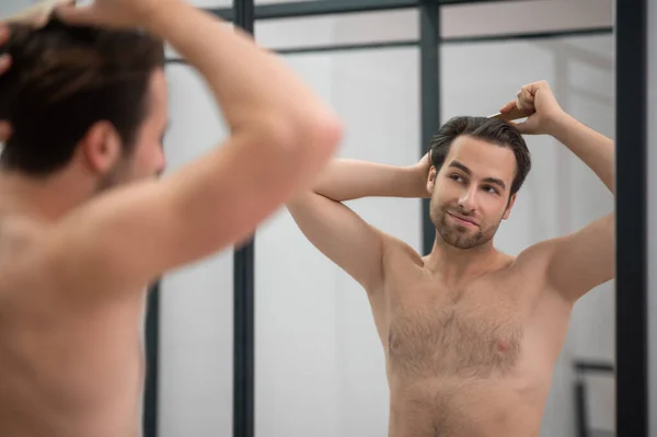 Темноволосый мужчина расчесывает волосы перед зеркалом — стоковое фото