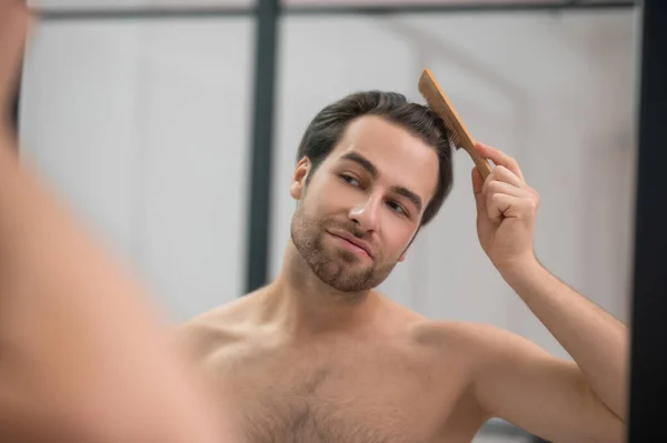 Young handsome man brushing his hair and looking contented — Stockfoto