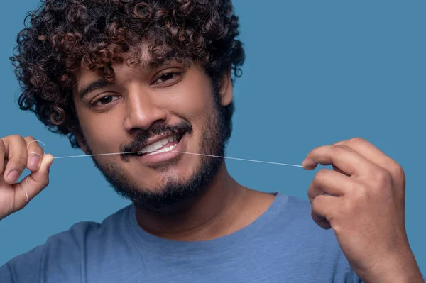 Smiling guy with curly hair flossing his teeth — Stock Photo, Image