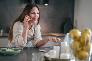 Mutfakta telefonla konuşan gülümseyen genç bir kadın.