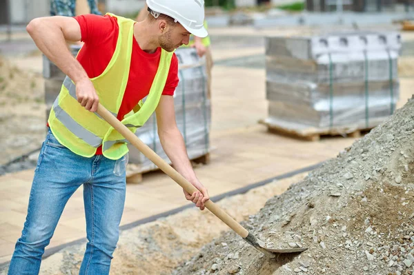 Kürekli bir adam inşaat alanından moloz topluyor.
