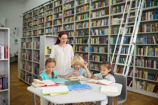 Woman watching children reading books at table — Stock Fotó