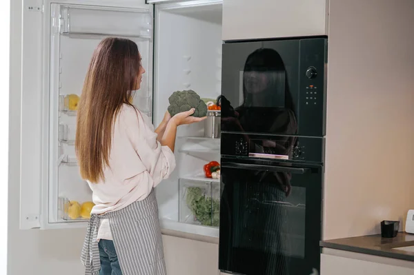 Jonge huisvrouw staat bij de koelkast in de keuken — Stockfoto