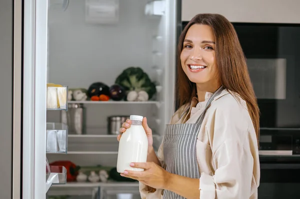 冷蔵庫から食べ物を取る若い女性 — ストック写真