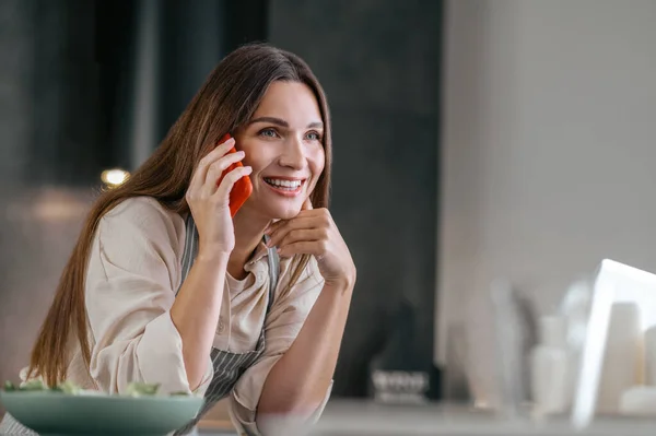 Joven mujer sonriente hablando por teléfono en la cocina — Foto de Stock