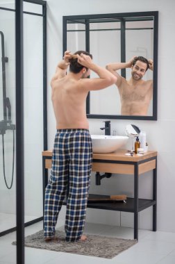 Ekose pantolonlu bir adam aynanın karşısında dikiliyor.