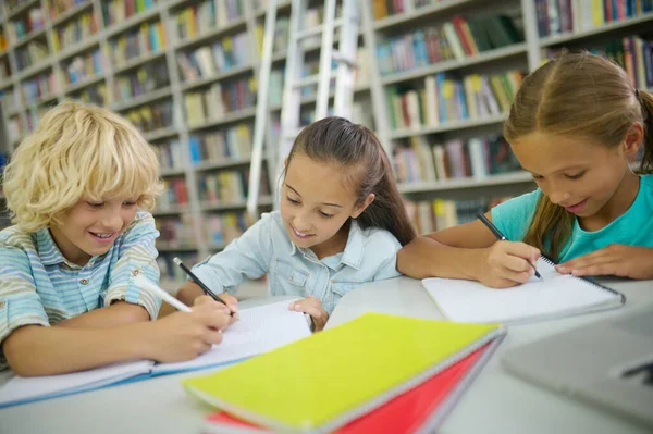 Niño y dos niñas escribiendo en la mesa —  Fotos de Stock