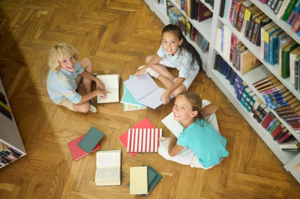 Children sitting on floor of library looking at camera — Fotografia de Stock