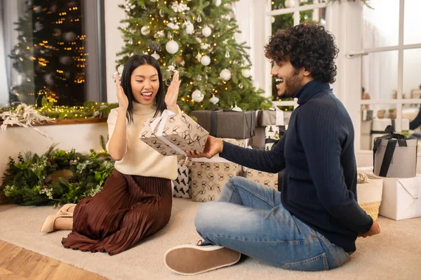 Man giving gift to enthusiastic woman sitting on floor — стоковое фото