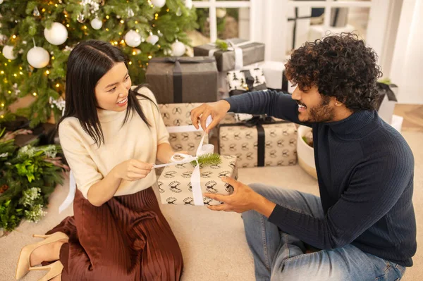 Женщина и мужчина открывают рождественский подарок сидя на полу — стоковое фото
