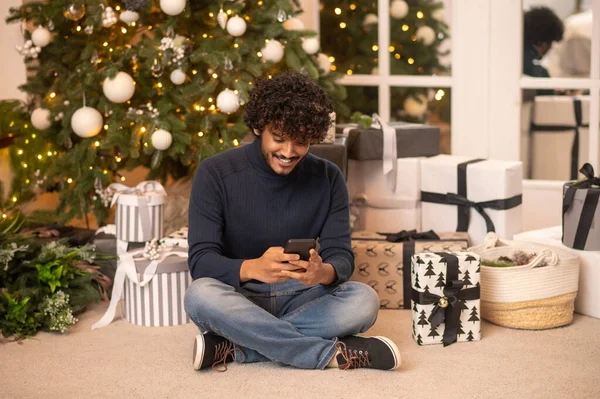 Vidám ember néz smartphone ül közel karácsonyfa — Stock Fotó