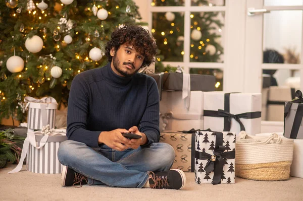 Man with smartphone sitting on floor looking at camera — Stock Fotó