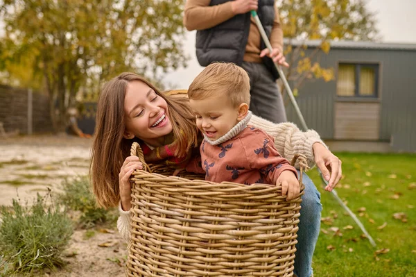 Woman playing with child sitting in basket in garden — Fotografia de Stock