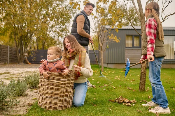 Femme accroupie touchant l'enfant dans le panier et la famille dans le jardin — Photo