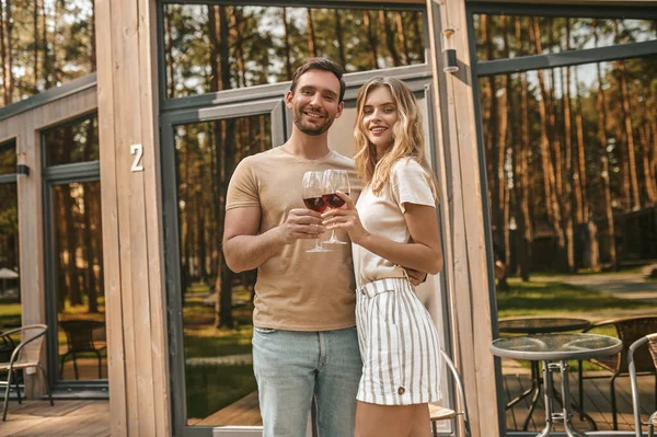 Νεαρό χαμογελαστό ζευγάρι που κρατάει ποτήρια με κρασί και δείχνει χαρούμενο — Φωτογραφία Αρχείου