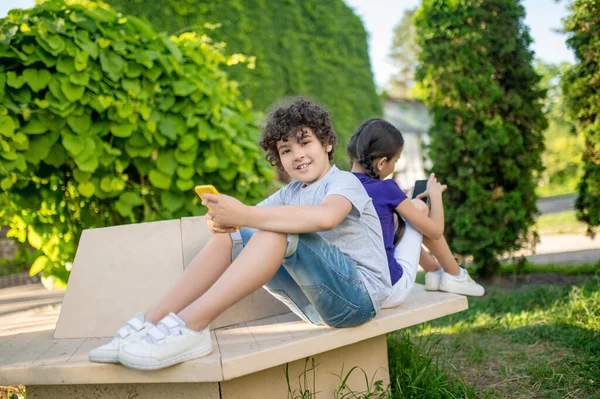 Deux enfants avec des téléphones portables assis dans le parc — Photo