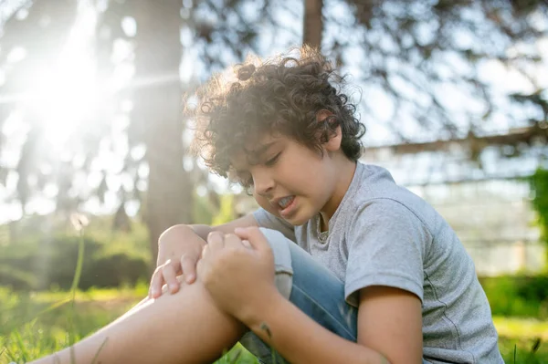 Concentré garçon brun examinant son genou endommagé — Photo