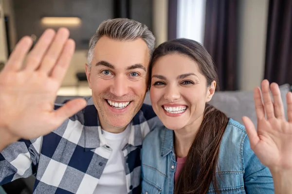 Man och kvinna med upphöjd hand tittar på kameran — Stockfoto